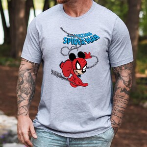 May include: A heather gray short-sleeve t-shirt featuring a graphic print of a character wearing a red and black spider-themed suit with mouse ears. Above the character, the text reads THE AMAZING SPIDER-MAN in blue letters with a web design.