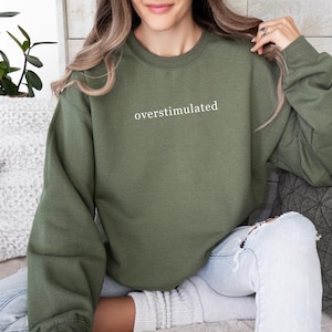 May include: A green sweatshirt with the text "overstimulated" printed in white on the front.
