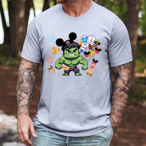 Puede incluir: Una camiseta gris con un Hulk de dibujos animados verde que lleva un sombrero de Mickey Mouse y sostiene globos con varios personajes de Disney. El texto "Save" est&aacute; impreso en la camiseta de Hulk.
