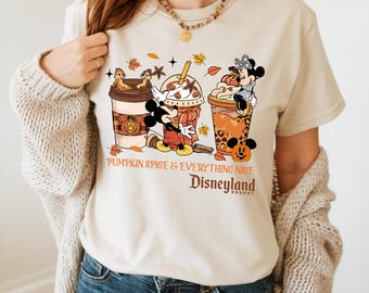 May include: Beige t-shirt featuring a graphic of Mickey and Minnie Mouse with fall-themed coffee cups. The text "Pumpkin Spice & Everything Nice" and "Disneyland Resort" are printed below the graphic. The shirt has short sleeves.