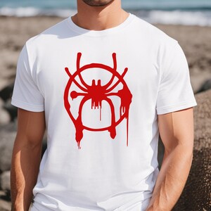 Puede incluir: Camiseta blanca con un gr&aacute;fico rojo de una ara&ntilde;a en un c&iacute;rculo. La ara&ntilde;a est&aacute; estilizada y tiene efectos de pintura que gotean.