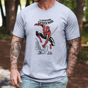May include: A gray t-shirt with a graphic of Spider-Man swinging through the city. The text "The Amazing Spider-Man" is printed above the graphic.