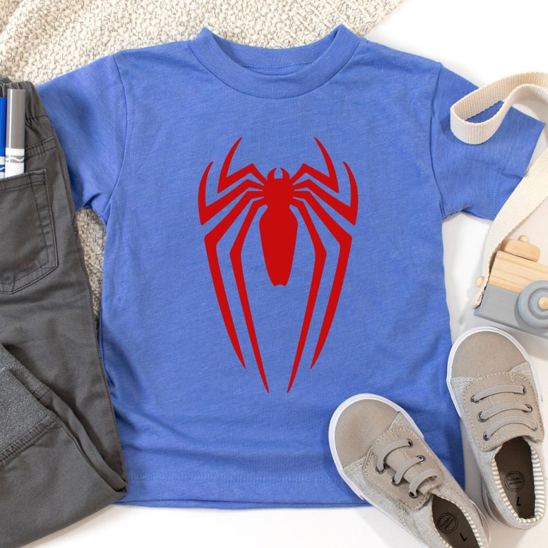 May include: A blue t-shirt with a red spider-man logo on the front.