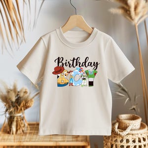 May include: A white t-shirt with a graphic of Toy Story characters spelling out "Birthday Boy".