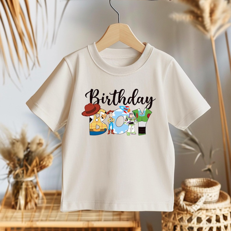 May include: A white t-shirt with a graphic of Toy Story characters spelling out "Birthday Boy".