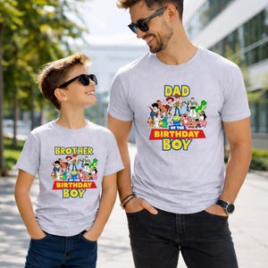 May include: Two light gray t-shirts with a colorful graphic of cartoon characters. One shirt reads "DAD OF THE BIRTHDAY BOY" and the other reads "BROTHER OF THE BIRTHDAY BOY". Both shirts have a red and yellow banner.