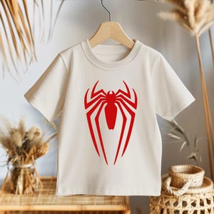 May include: White t-shirt with a red spider-man logo printed on the front.