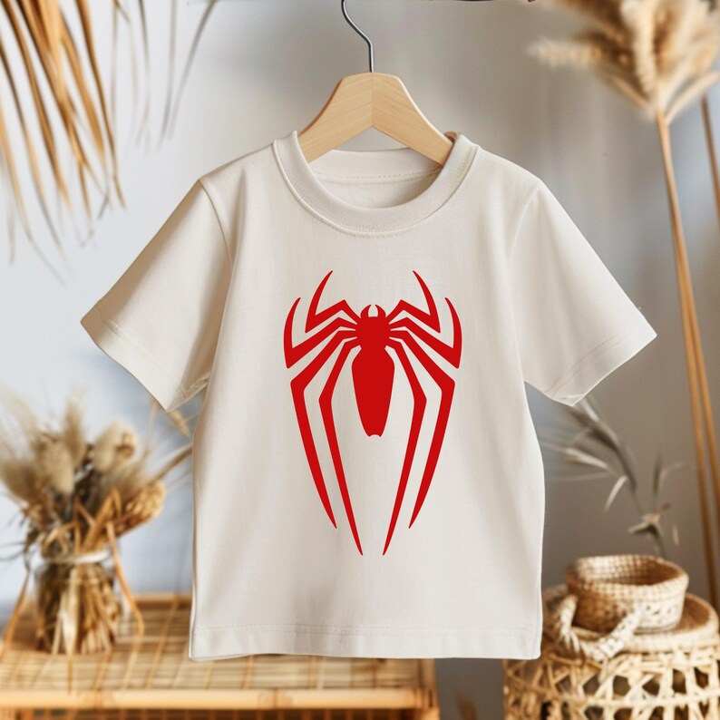 May include: White t-shirt with a red spider-man logo printed on the front.