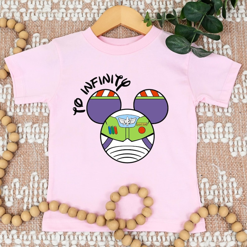 May include: Pink short-sleeved t-shirt with a black graphic of a Mickey Mouse head with Buzz Lightyear's helmet and the text "To Infinity".