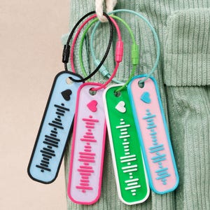 May include: A set of keychains in various colours, each with a music-themed design. The keychains feature a heart symbol and a barcode-like pattern. The colour schemes include blue, pink, and green. They are attached to a metal loop.