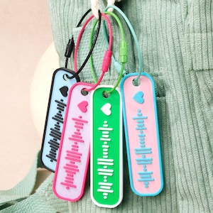 Può includere: Quattro portachiavi colorati con design a cuore e onda sonora in blu, rosa, verde e rosa con dettagli blu. Sono attaccati a un cordino verde.