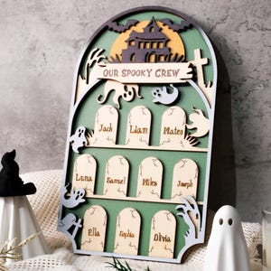 Peut inclure: Décoration d'Halloween en bois avec un fond vert et une silhouette de maison hantée. Le panneau indique "OUR SPOOKY CREW" et comporte des découpes de pierres tombales avec des noms. Comprend des décorations de fantômes et de chapeaux de sorcière.