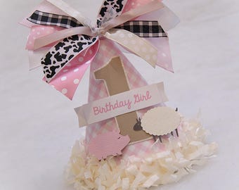 May include: Pink and white gingham party hat with a number one, a pig and a sheep, and a white ribbon with the text "Birthday Girl".