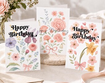 May include: Three white greeting cards with watercolor floral illustrations and the text Happy Birthday. The left card features purple and pink flowers, the center card shows pink carnations with a bow, and the right card displays yellow daffodils.