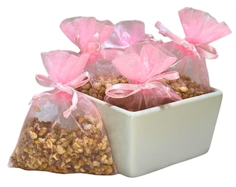 May include: A white ceramic bowl filled with pink tulle bags containing dried fruit and herbs. The bags are tied with pink ribbon.