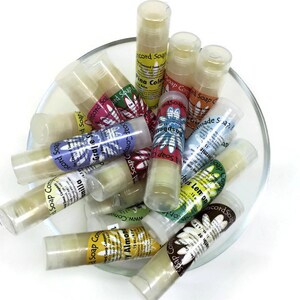 May include: A glass bowl filled with various small, clear tubes of lip balm. Each tube has a colorful label with a floral design and text that includes "Concord Soap Company" and the scent of the balm, such as "Vanilla", "Grape", and "Lemon".