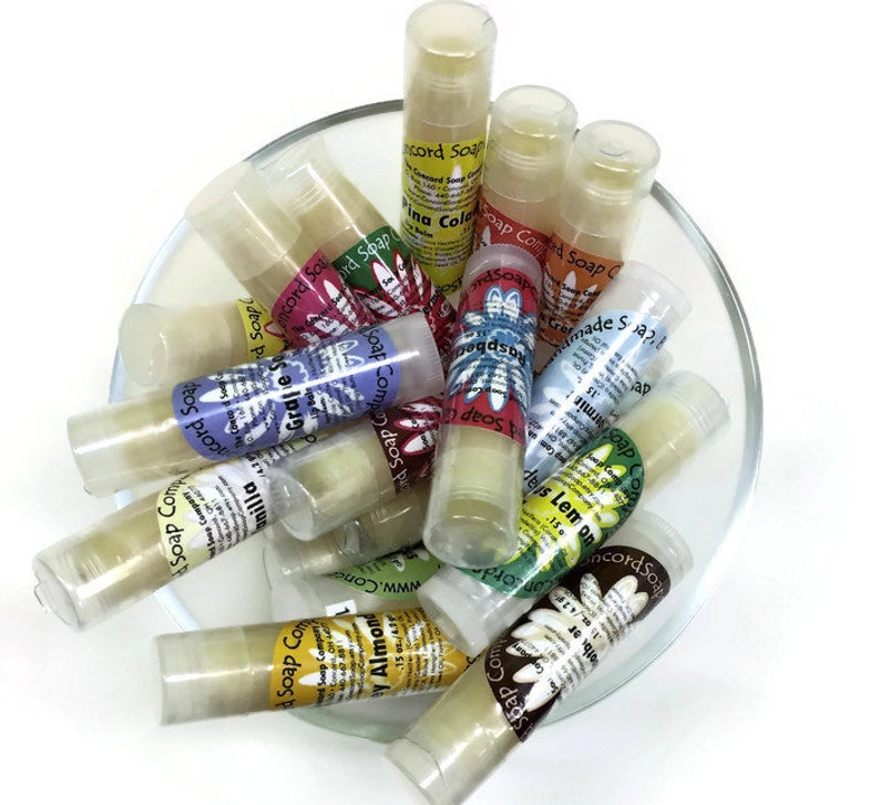 May include: A glass bowl filled with various small, clear tubes of lip balm. Each tube has a colorful label with a floral design and text that includes "Concord Soap Company" and the scent of the balm, such as "Vanilla", "Grape", and "Lemon".