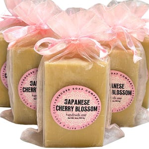May include: Three bars of handmade soap wrapped in pink tulle bags. The soap is a light yellow color and has a label that reads "Japanese Cherry Blossom Handmade Soap".