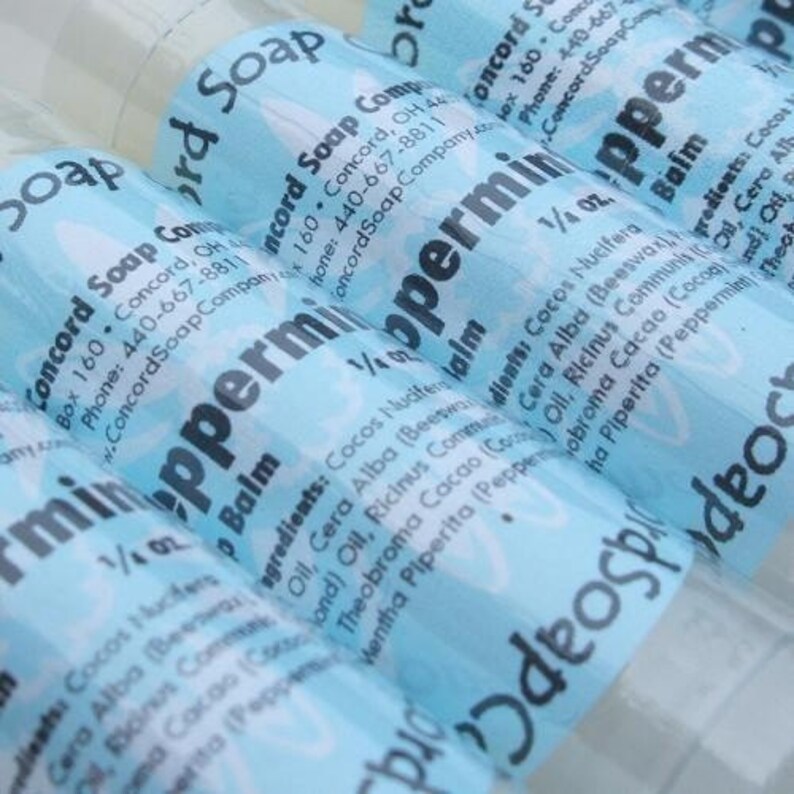 May include: A close-up of three blue and white labeled tubes of peppermint balm. The labels feature the text "Peppermint Balm" and list the ingredients: Cocos Nucifera, Cera Alba, Ricinus Communis Oil, Theobroma Cacao, Mentha Piperita. The labels also include the company name and contact information: Concord Soap Company, Box 160, Concord, OH 44077, Phone: 440-667-8811.