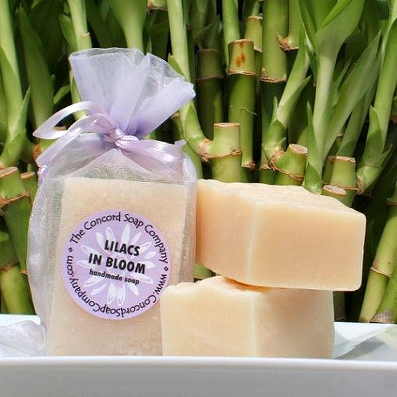May include: Two bars of handmade soap wrapped in a lavender sheer bag. The soap is white and the label reads 'The Concord Soap Company, Lilacs in Bloom, handmade soap'.