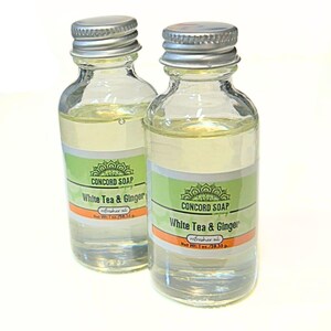 May include: Two clear glass bottles with silver caps, filled with a light yellow liquid. Each bottle has a green and white label with the text "CONCORD SOAP White Tea & Ginger refresher oil". The net weight is 1 oz / 28.35 g.