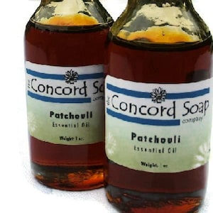 May include: Two amber glass bottles with brown liquid inside. Both bottles have a white label with green accents and the text "Concord Soap Company" and "Patchouli Essential Oil" printed on them. The label on the left bottle says "Weight 1 oz." and the label on the right bottle says "Weight 1 oz."