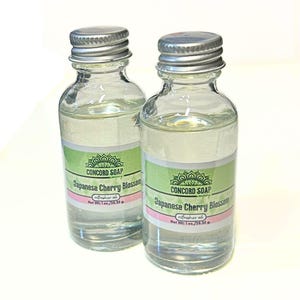 May include: Two clear glass bottles with silver caps, filled with a clear liquid. Each bottle has a green and pink label that reads "CONCORD SOAP Japanese Cherry Blossom refresher oil" and "Net Wt. 1 oz./28.35 g."