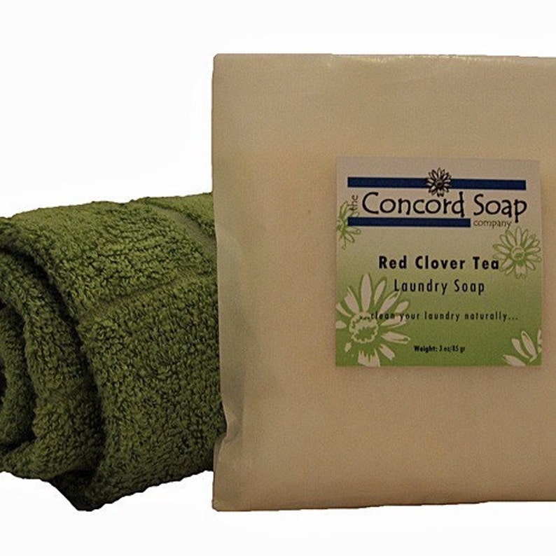 May include: A bar of white laundry soap with a green and white label that reads "The Concord Soap Company Red Clover Tea Laundry Soap Clean your laundry naturally... Weight: 3 oz/85 g" and a green rolled up towel.