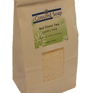 May include: A white paper bag with a brown paper flap. The bag has a label that says "Concord Soap Company" and "Red Clover Tea Laundry Soap". The label also says "Clean your laundry naturally..." and "Weight: 12 oz (340.2 g)".