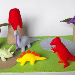 May include: A felt play set with a red volcano, a green palm tree, a purple pterodactyl, a blue dinosaur, a yellow dinosaur, a green triceratops, and a red T-Rex dinosaur.