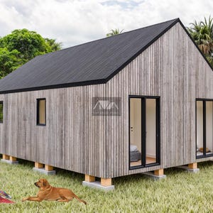 K&ouml;nnte beinhalten: Ein kleines, modernes, graues Holzhaus mit einem schwarzen Dach und gro&szlig;en Fenstern. Das Haus steht auf einem Fundament aus Betonbl&ouml;cken und ist von gr&uuml;nem Gras und B&auml;umen umgeben. Zwei Personen sitzen auf einer roten Decke vor dem Haus, und ein Hund liegt im Gras.