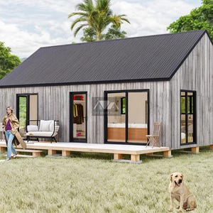 K&ouml;nnte beinhalten: Eine kleine, moderne, graue und schwarze H&uuml;tte mit einer Holzterrasse und einem Hund im Vordergrund. Die H&uuml;tte hat gro&szlig;e Fenster und ein schwarzes Dach. Der Hund ist hellbraun und sitzt auf dem Gras.