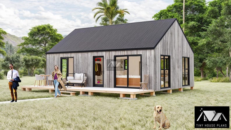 K&ouml;nnte beinhalten: Eine kleine, moderne, graue und schwarze H&uuml;tte mit einer Holzterrasse und einem Hund im Vordergrund. Die H&uuml;tte hat gro&szlig;e Fenster und ein schwarzes Dach. Der Hund ist hellbraun und sitzt auf dem Gras.