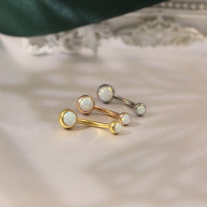 May include: Three belly button rings with opal stones. The rings are gold, rose gold, and silver.