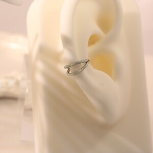 May include: A silver ear cuff with a white opal design. The cuff is worn on a mannequin's ear.