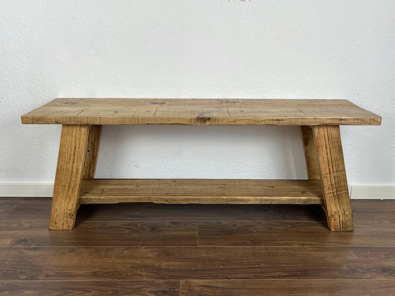 May include: A rustic wooden bench with a lower shelf. The bench is made of natural wood with a light brown finish. The bench has a simple design with straight legs and a rectangular top.