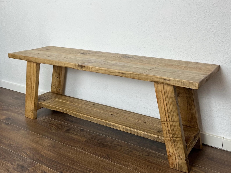 May include: A rustic wooden bench with a shelf. The bench is made of natural wood with a light brown finish. The shelf is located below the seat and is also made of wood.