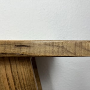 May include: A wooden table with a natural finish and a rectangular top. The table has a simple, rustic design with a slightly uneven surface.