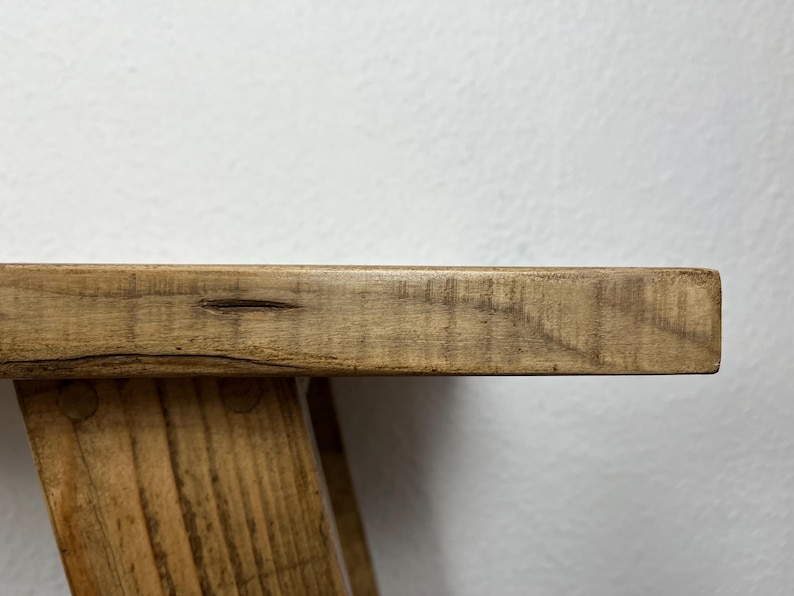 May include: A wooden table with a natural finish and a rectangular top. The table has a simple, rustic design with a slightly uneven surface.