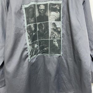 May include: A dark gray long-sleeve button-down shirt with a black and white collage of monster movie characters on the back.