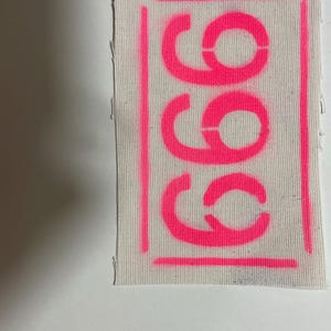 May include: A white fabric patch with a pink outline and the word "COCO" written in pink letters.