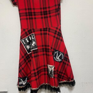 May include: Red and black plaid dress with a black tulle ruffle hem and various punk rock band patches, including "T.S.O.L." and "Stiff Little Fingers".