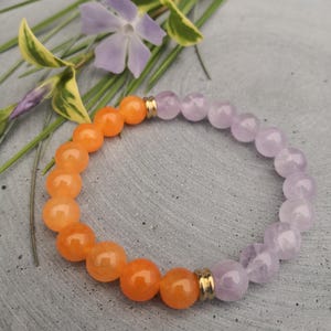 Könnte beinhalten: Ein Armband aus orangefarbenen und violetten Perlen. Das Armband hat goldene Akzente.