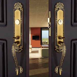 May include: Ornate brass door handles with intricate floral designs. The handles are mounted on a dark brown door, with a glimpse of the interior visible through the open doorway. The door hardware has a vintage aesthetic.