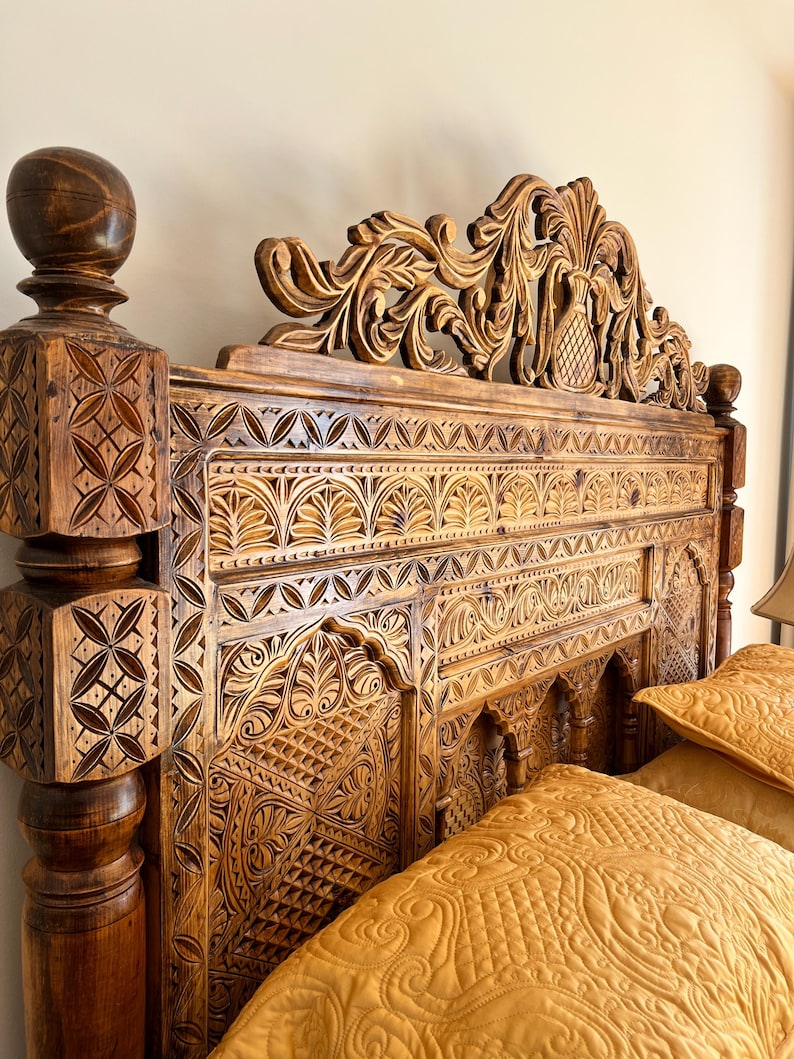 May include: A dark brown wooden headboard featuring intricate hand-carved geometric and floral patterns. The headboard includes a tall, ornate crest with a central pineapple motif and square corner posts topped with spherical finials.