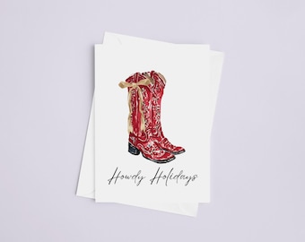 Pode incluir: Cartão com uma ilustração em aquarela de botas de cowboy vermelhas com estampas florais e laços bege. As palavras "Howdy Holidays" estão escritas em uma fonte de script abaixo. O cartão está em um fundo branco.