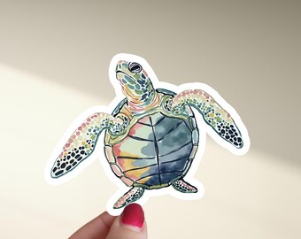 May include: A colorful watercolor sticker of a sea turtle. The turtle has a green and blue shell with yellow, pink, and orange accents. Its flippers are outstretched, and the sticker is on a white background.