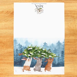 Pode incluir: Ilustra&ccedil;&atilde;o em aquarela de tr&ecirc;s coelhos carregando uma &aacute;rvore de Natal por uma floresta nevada. A parte superior do papel tem o texto "MVA" e um desenho floral. O fundo apresenta uma floresta em aquarela.