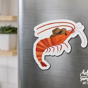 May include: A red shrimp wearing a brown cowboy hat. The shrimp is on a white background with the text "hello summer art studio" in black.