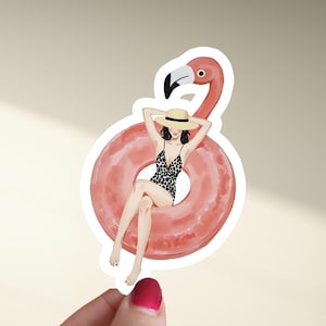 Könnte beinhalten: Aufkleber mit einer Frau in einem Leoparden-Badeanzug und Strohhut, die sich auf einem rosa Flamingo-Schwimmring entspannt. Der Flamingo hat einen langen Hals und einen schwarz-weißen Schnabel. Der Aufkleber befindet sich auf weißem Hintergrund.